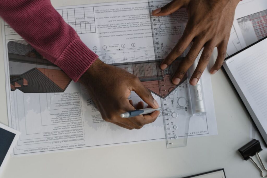 pexels-photo-6614837 Architect sketching on blueprints with ruler at desk, designing a building layout.
